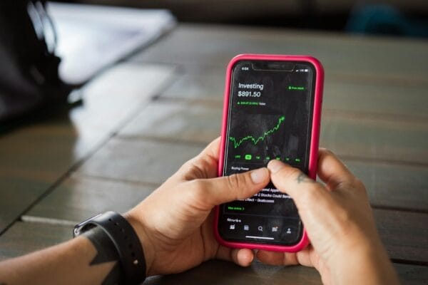 A person holding a smartphone with a stock market app displaying analytics and stock prices.