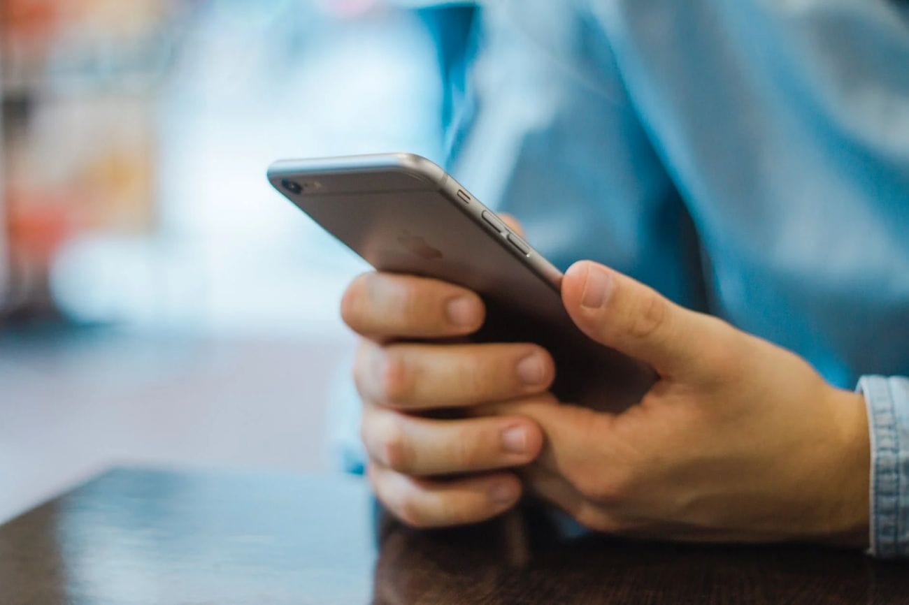 Someone wearing a light blue shirt is sitting at a table holding a smartphone, possibly checking their website on it. The background is blurry, which makes the person’s hands and phone stand out, highlighting how important staying connected is in today’s business world.