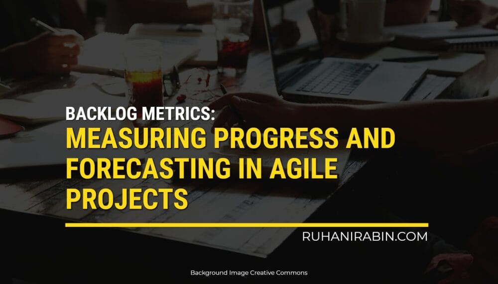 A table with laptops, drinks, and paperwork. The screen says: "Backlog Metrics: Tracking Progress and Predicting Outcomes in Agile Project Management" by RuhaniRabin.com.